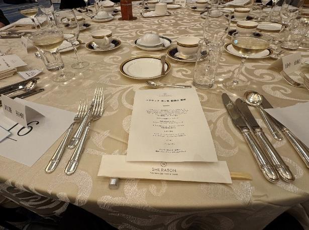 懇親会会場の円卓に並べられたコース料理の食器とメニュー表。シェラトンのロゴ入り割り箸袋が置かれている。