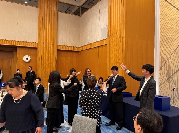 経営方針説明会後の懇親会で行われたじゃんけん大会。壇上付近で数人がじゃんけんの手を出して盛り上がっている場面。